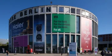 نمای بیرونی ساختمان مدور مرکز همایشهای Messe Berlin با بنرهای تبلیغاتی بزرگ شرکتهای هایر، اسنپدراگون و لوگوی نمایشگاه IFA در روز آفتابی.