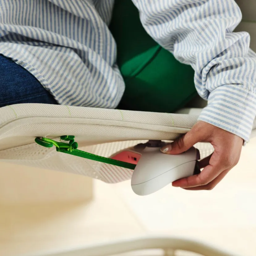 نمای نزدیک از قسمت زیرین صندلی راحتی سفید مجموعه IKEA و Xbox که محفظه نگهداری، کابل سبز و دست یک فرد در حال تنظیم یا اتصال تجهیزات را نشان میدهد.
