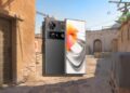 تصویر گوشی هوشمند نوبیا با بدنه پشتی خاکستری تیره و ماژول دوربین بزرگ مشکیرنگ Nubia در کنار پنل جلویی با نمایشگر تمامصفحه و حاشیههای بسیار باریک، در پسزمینهای از یک نقشه بازی تیراندازی سهبعدی و قدیمی.