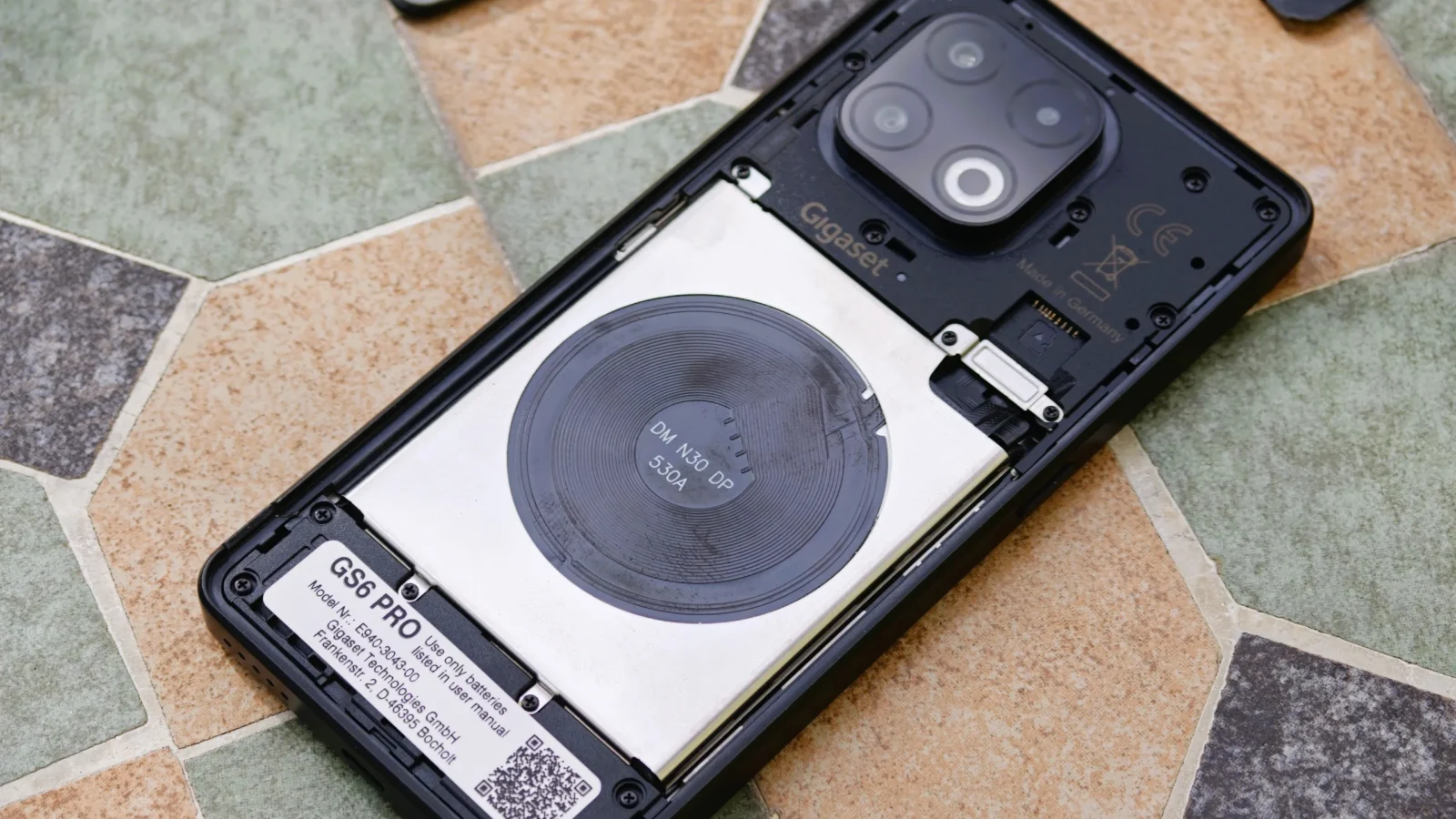 نمای داخلی و بدون قاب گوشی گیگاست GS6 Pro با باتری قابل تعویض، سیمپیچ شارژ بیسیم و برچسب مشخصات ساخت آلمان.