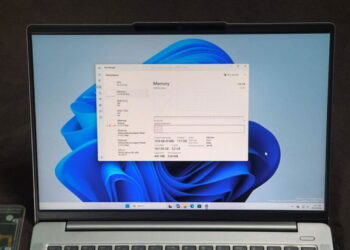 نمای روبرو از نمایشگر لپ‌تاپ نقره‌ای با والپیپر آبی ویندوز ۱۱ و پنجره باز Task Manager در تب Performance، که بخش Memory با ظرفیت کل ۱۲۸ گیگابایت را نشان می‌دهد.