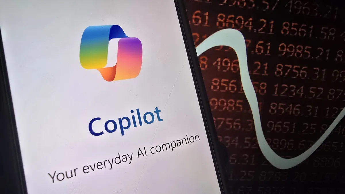 نمای نزدیک از صفحه ای که لوگوی Copilot و عبارت “Your everyday AI companion” را نشان می دهد و در کنار آن بخشی از نمودار و اعداد نارنجی روی پس زمینه تیره دیده می شود.