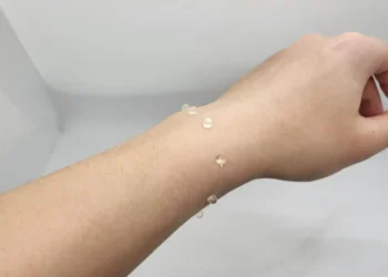 نمونه اولیه رشته الکترونیکی شفاف و انعطاف‌پذیر نصب‌شده روی مچ دست برای پایش پزشکی پوشیدنی و ثبت مداوم داده‌های سلامت.