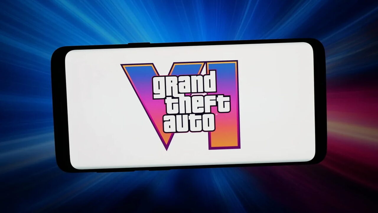 لوگوی Grand Theft Auto VI روی نمایشگر سفید یک گوشی هوشمند، با پس‌زمینه‌ای از پرتوهای نور آبی، صورتی و قرمز.