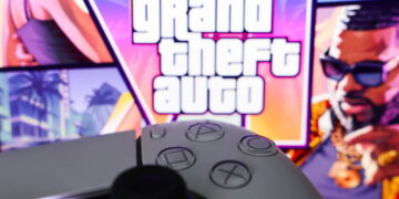 کنترلر مشکی کنسول در پیشزمینه و لوگوی بزرگ Grand Theft Auto با تصاویر رنگارنگ شخصیتها و فضای ساحلی GTA 6 در پسزمینه.