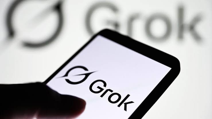 نمای نزدیک از یک دستگاه لمسی که لوگوی Grok را روی صفحه نمایش میدهد و انگشت کاربر در بخش پایین تصویر به صفحه اشاره میکند؛ عبارت Grok در پسزمینه نیز دیده میشود.