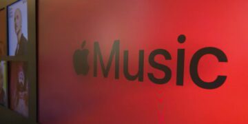 نمای نزدیک از لوگوی Apple Music با نماد اپل و عبارت Music روی پسزمینهای قرمز و نورپردازیشده.