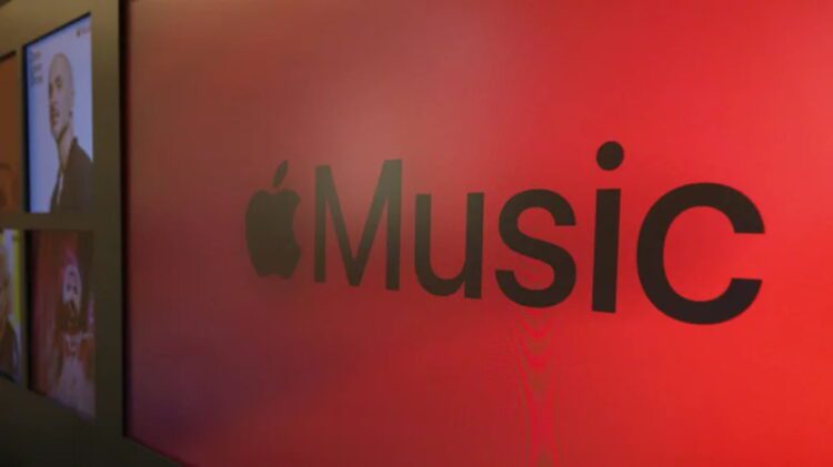 نمای نزدیک از لوگوی Apple Music با نماد اپل و عبارت Music روی پسزمینهای قرمز و نورپردازیشده.