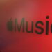 نمای نزدیک از لوگوی Apple Music با نماد اپل و عبارت Music روی پسزمینهای قرمز و نورپردازیشده.