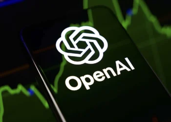 لوگوی شرکت OpenAI روی تلفن همراه در کنار نمودارهای مالی