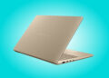 نمای مایل از پشت درپوش بژ مات لپتاپ ایسوس زنبوک با لوگوی متنی ASUS Zenbook در پسزمینهای به رنگ آبی فیروزهای.