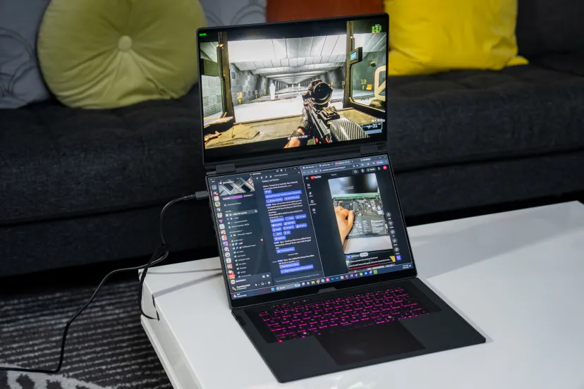 لپتاپ گیمینگ ایسوس سری ROG با نورپردازی RGB کیبورد، در حال اجرای بازی شوتر در نمایشگر اصلی و برنامههای دیسکورد و یوتیوب در صفحه دوم.