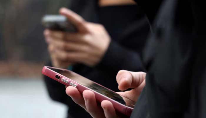 نمای نزدیک از دست دو فرد در حال استفاده و تایپ با گوشیهای هوشمند با کاورهای صورتی و مشکی