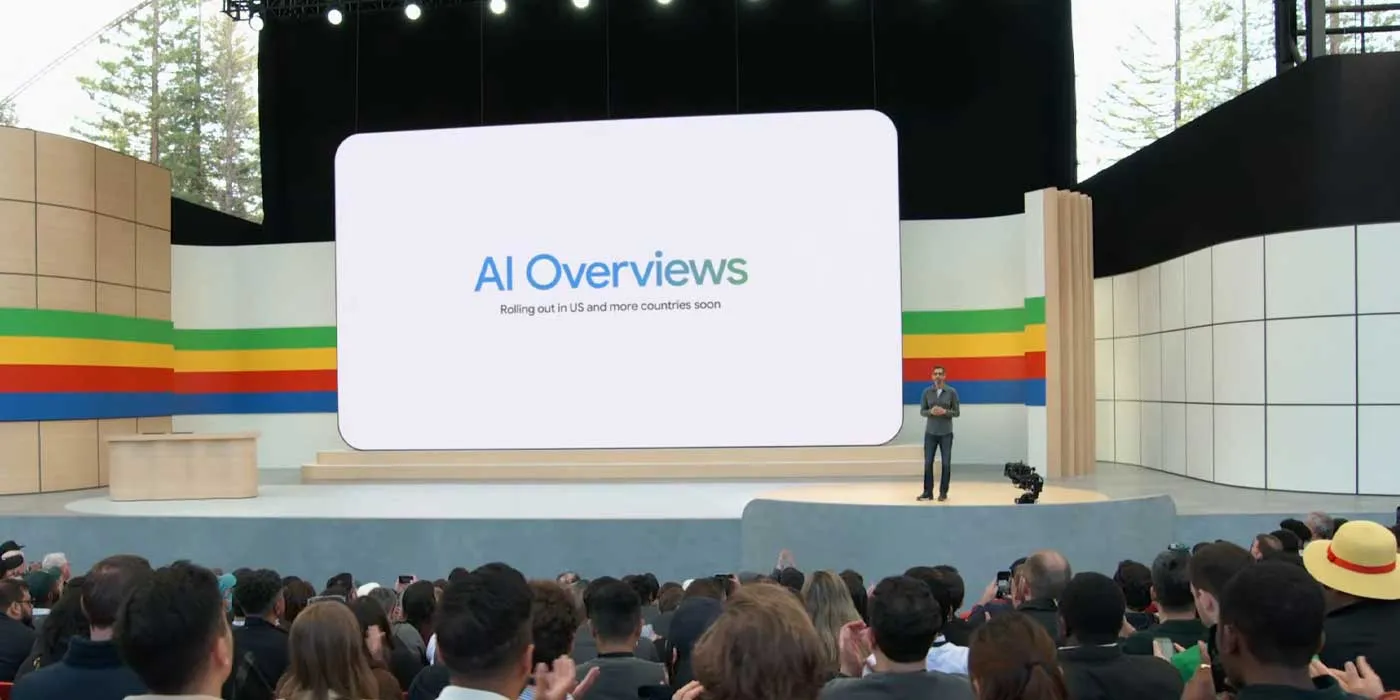 سوندار پیچای روی استیج رویداد گوگل در برابر حضار در حال معرفی بخش جستوجوی هوشمند AI Overviews روی صفحه نمایش بزرگ سالن