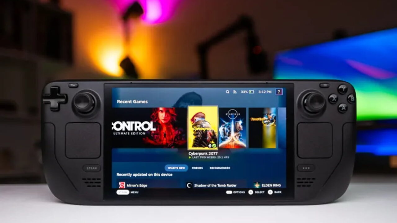 کنسول بازی دستی Steam Deck مشکی با نمایشگر روشن در حال اجرای منوی بازیها شامل Cyberpunk 2077 روی میز
