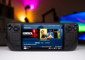 کنسول بازی دستی Steam Deck مشکی با نمایشگر روشن در حال اجرای منوی بازی‌ها شامل Cyberpunk 2077 روی میز