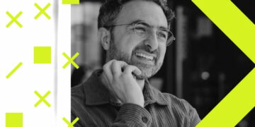پرتره سیاه و سفید مصطفی سلیمان خندان با موهای کمی جوگندمی، عینک گرد نازک و ریش کوتاه که در حالت فکری دستش را زیر چانهاش گذاشته، در قالب طراحی گرافیکی با اشکال هندسی لیمویی مانند ضربدر و مربع