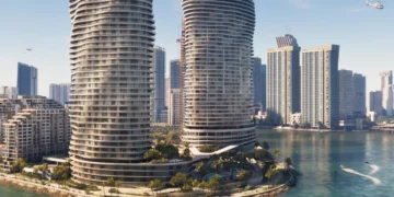 نمای سینمایی برجهای مسکونی دو قلوی موجدار شیشهای Vice City در پسزمینه آسمان آبی صاف، با برجهای مسکونی شهر در پسزمینه، درختان نخل روی برآمدگیهای جزیره و قایقهای متحرک در آبهای فیروزهای روشن؛ پلهای طولانی در افق دوردست دیده میشوند و یک بالگرد در پرواز است.