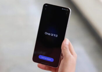 در دست گرفتن گوشی سامسونگ گلکسی S26 FE با نمایش عبارت One UI 9.0 روی صفحه‌نمایش تاریک
