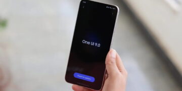 در دست گرفتن گوشی سامسونگ گلکسی S26 FE با نمایش عبارت One UI 9.0 روی صفحه‌نمایش تاریک