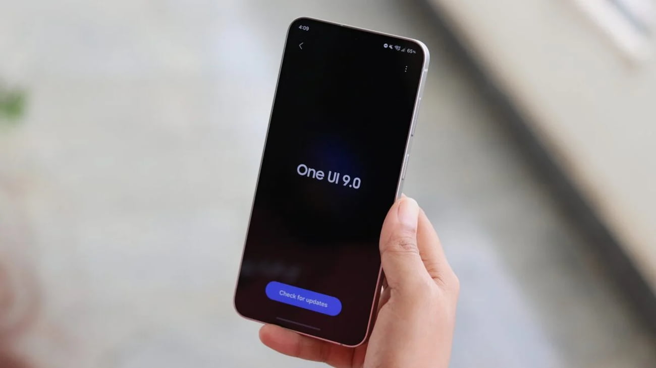 در دست گرفتن گوشی سامسونگ گلکسی S26 FE با نمایش عبارت One UI 9.0 روی صفحهنمایش تاریک