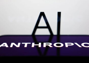 نمای افقی صفحه‌نمایش یک گوشی هوشمند با لوگوی سفید تایپوگرافی شرکت ANTHROPIC روی پس‌زمینه بنفش در پیش‌زمینه، با حروف بزرگ AI در پس‌زمینه تار و سفید.