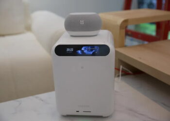 دستگاه ذخیره‌ساز سفید رنگ UGREEN به همراه نمایشگر کوچک جلویی و ساعت دیجیتال با بلندگوی هوشمند قرار گرفته روی آن در دکوراسیون اتاق.