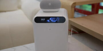 دستگاه ذخیرهساز سفید رنگ UGREEN به همراه نمایشگر کوچک جلویی و ساعت دیجیتال با بلندگوی هوشمند قرار گرفته روی آن در دکوراسیون اتاق.