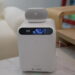 دستگاه ذخیرهساز سفید رنگ UGREEN به همراه نمایشگر کوچک جلویی و ساعت دیجیتال با بلندگوی هوشمند قرار گرفته روی آن در دکوراسیون اتاق.