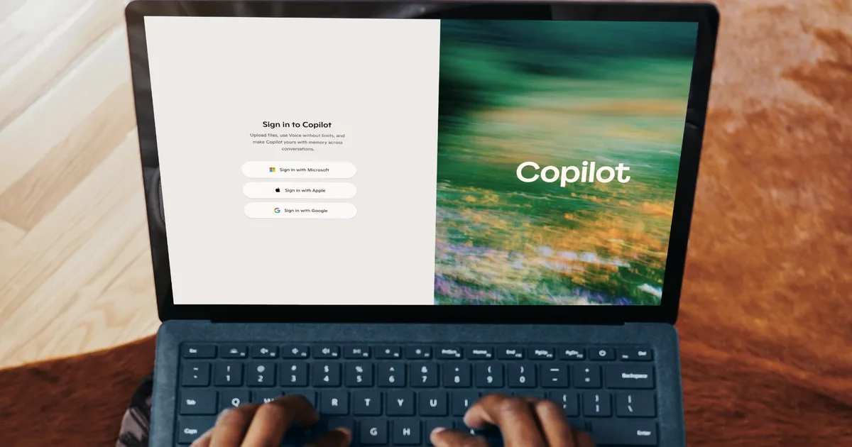 دستها در حال تایپ روی لپتاپ Microsoft Surface با صفحهی ورود به سایت Microsoft Copilot شامل گزینههای ورود با Microsoft، Apple و Google