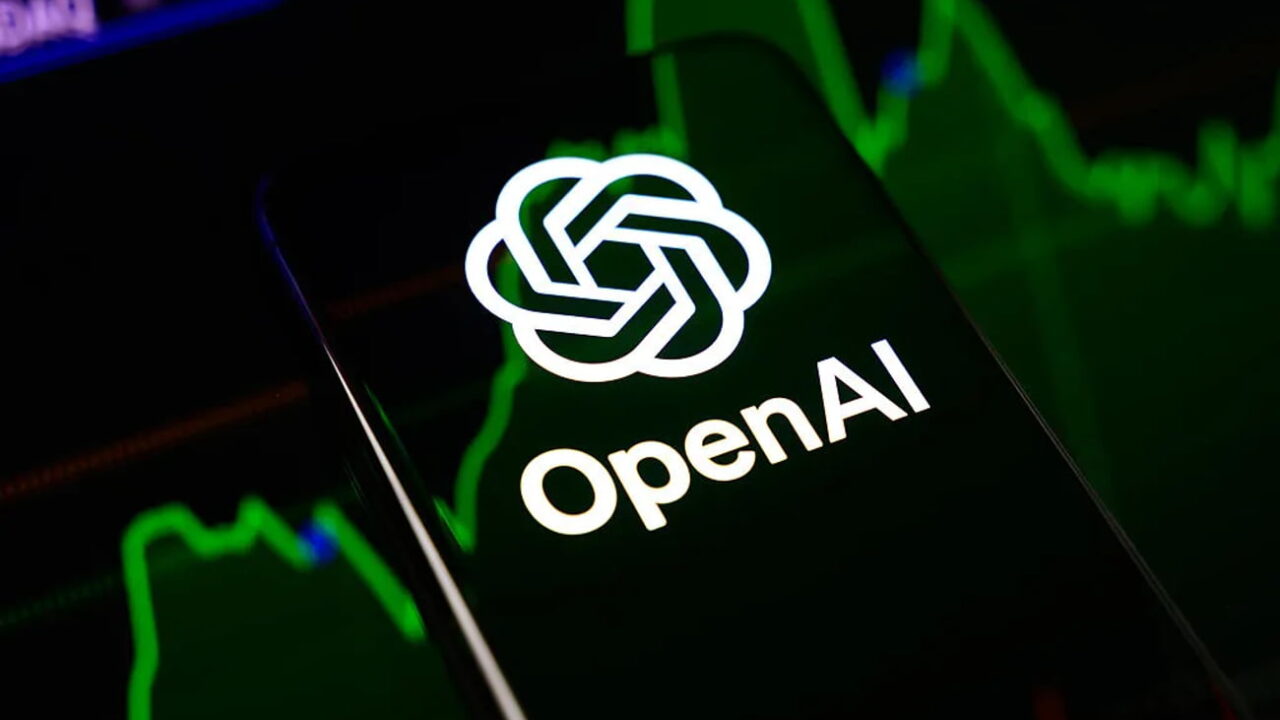 گوشی هوشمند با لوگوی سفید و نام OpenAI روی صفحه نمایش در مقابل پسزمینه سبز و تیره نمودارهای بازارهای مالی.