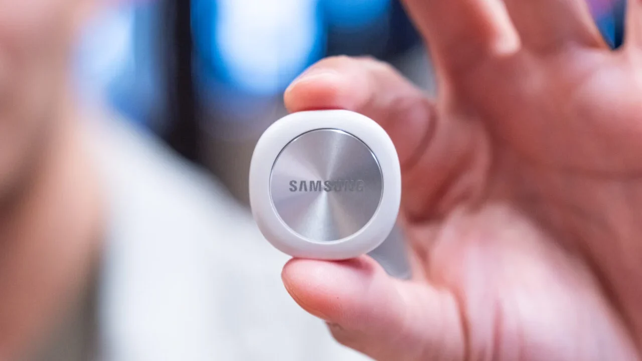 ردیاب هوشمند سفید سامسونگ با بخش میانی فلزی چرخان و لوگوی Samsung که بین انگشتان دست نگه داشته شده است.