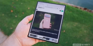 نمای دستی که تبلت تاشده Samsung Galaxy Z Fold 8 Ultra را در حالت باز نگرفته؛ صفحه نمایش نمایش وبسایت اندروید اتوریتی در مادهی ۲۵.۳ با مقاله Pixel 11 Pro در حاشیه سبز محو و بعد از پسزمینه.