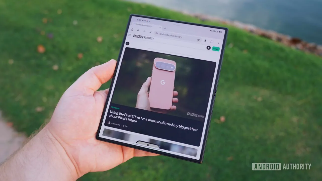 نمای دستی که تبلت تاشده Samsung Galaxy Z Fold 8 Ultra را در حالت باز نگرفته؛ صفحه نمایش نمایش وبسایت اندروید اتوریتی در مادهی ۲۵.۳ با مقاله Pixel 11 Pro در حاشیه سبز محو و بعد از پسزمینه.