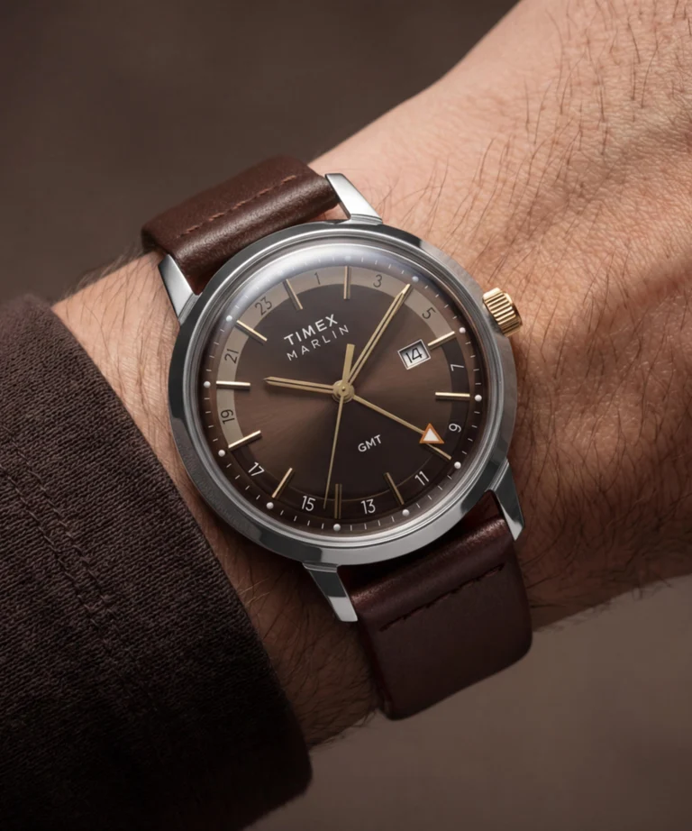 نمای ساعت مچی Timex Marlin GMT روی دست با صفحه قهوهای سانبرست، عقربههای طلایی و بند چرمی قهوهای تیره