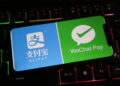 یک گوشی هوشمند روی صفحهکلید گیمینگ با نور پسزمینه رنگی که لوگوهای Alipay و WeChat Pay را روی نمایشگر خود نشان میدهد.