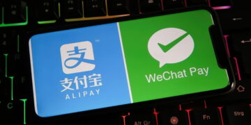 یک گوشی هوشمند روی صفحهکلید گیمینگ با نور پسزمینه رنگی که لوگوهای Alipay و WeChat Pay را روی نمایشگر خود نشان میدهد.