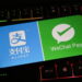 یک گوشی هوشمند روی صفحه‌کلید گیمینگ با نور پس‌زمینه رنگی که لوگوهای Alipay و WeChat Pay را روی نمایشگر خود نشان می‌دهد.
