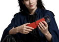 زنی با بارانی سرمهای رنگ که یک گوشی هوشمند متصل به ماژول گیتار جیبی قرمز را در دست گرفته و در حال استفاده از آن است.