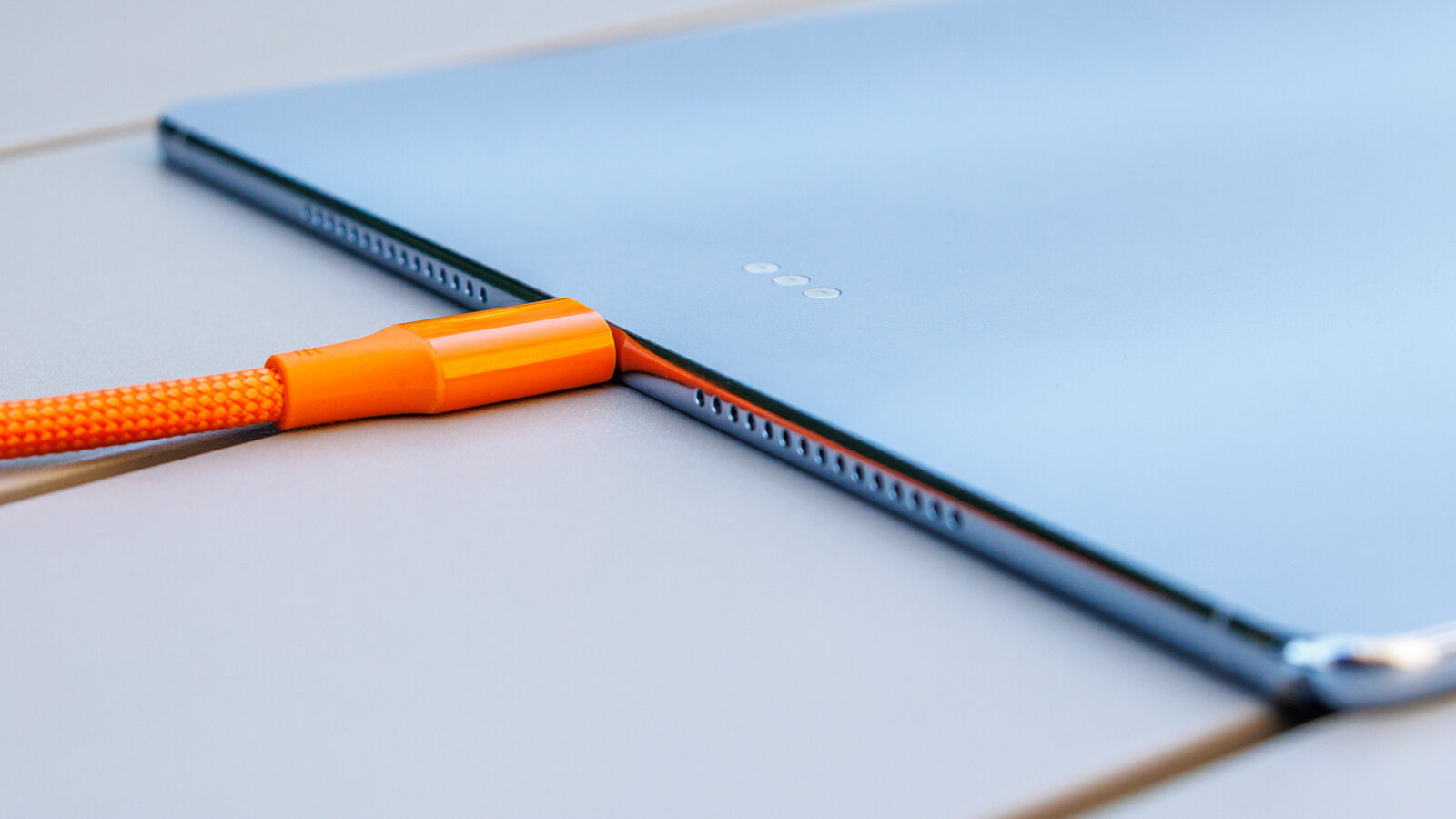 نمای جانبی تبلت هواوی MatePad Pro Max در حالت شارژ با کابل بافتدار نارنجی متصل به پورت USB-C، همراه با دکمههای کناری و بلندگوهای سوراخدار روی لبه بدنه.