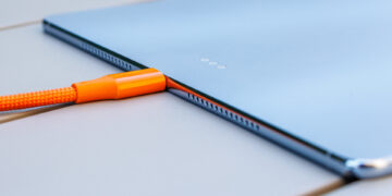 نمای جانبی تبلت هواوی MatePad Pro Max در حالت شارژ با کابل بافتدار نارنجی متصل به پورت USB-C، همراه با دکمههای کناری و بلندگوهای سوراخدار روی لبه بدنه.
