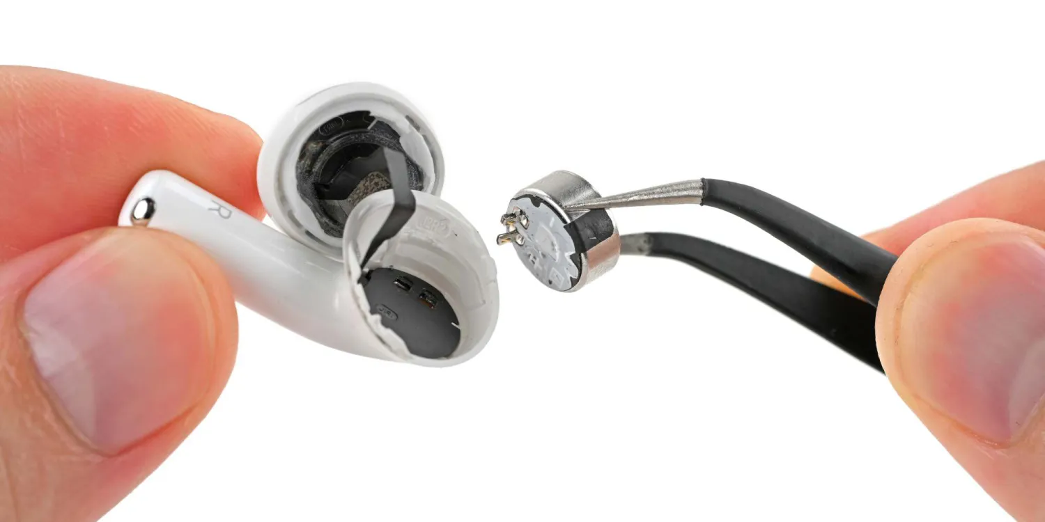 عکس کلوزآپ از جداسازی قطعات AirPods 5. دستی یک ایرباد سفید با پوسته شکافته را نگه داشته و با پنس مشکی، درایور بلندگوی نقرهای کوچک را از داخل آن بیرون میکشد. پسزمینه تصویر کاملاً سفید است.