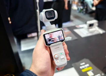 نمای کامل از دوربین گیمبال‌دار Insta360 Luna سفید رنگ در دست کاربر با نمایشگر روشن و کادربندی تصویر سلفی به همراه دکمه‌های کنترلی بدنه.