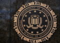 نشان رسمی وزارت دادگستری آمریکا و اداره تحقیقات فدرال FBI روی دیوار سنگی تیره، با عبارت‌های Department of Justice و Federal Bureau of Investigation.