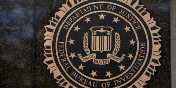 نشان رسمی وزارت دادگستری آمریکا و اداره تحقیقات فدرال FBI روی دیوار سنگی تیره، با عبارت‌های Department of Justice و Federal Bureau of Investigation.