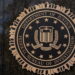 نشان رسمی وزارت دادگستری آمریکا و اداره تحقیقات فدرال FBI روی دیوار سنگی تیره، با عبارتهای Department of Justice و Federal Bureau of Investigation.