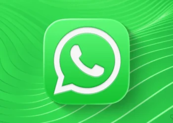 لوگوی واتساپ در مرکز تصویر؛ آیکون سبز گرد روی پس‌زمینه سبز موج‌دار با خطوط منحنی و واترمارک 9to5Mac در گوشه پایین راست.
