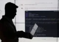 سیلوئت یک شخص در حال کار با لپ‌تاپ در برابر یک نمایشگر بزرگ که کدهای پایتون (PyTorch CNN) روی آن نمایش داده شده است.