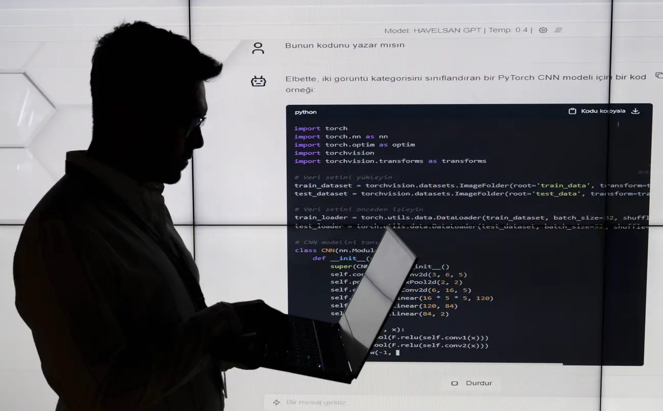 سیلوئت یک شخص در حال کار با لپتاپ در برابر یک نمایشگر بزرگ که کدهای پایتون (PyTorch CNN) روی آن نمایش داده شده است.