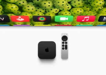 دستگاه Apple TV مشکی‌رنگ و ریموت کنترل آن روی سطحی سفید در کنار بخشی از تلویزیون که رابط کاربری tvOS و آیکون برنامه‌های مختلف را نشان می‌دهد.